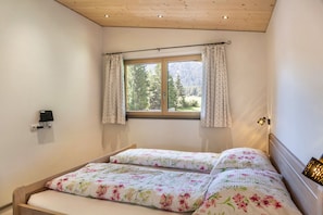 Una camera da letto con soffitto in legno, una finestra con tende, un letto con biancheria da letto a fiori e un lampadario fissato al muro.