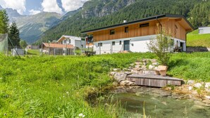 Ein modernes Haus mit Holzfassade, einem kleinen Teich und einer Bergkulisse im Hintergrund.