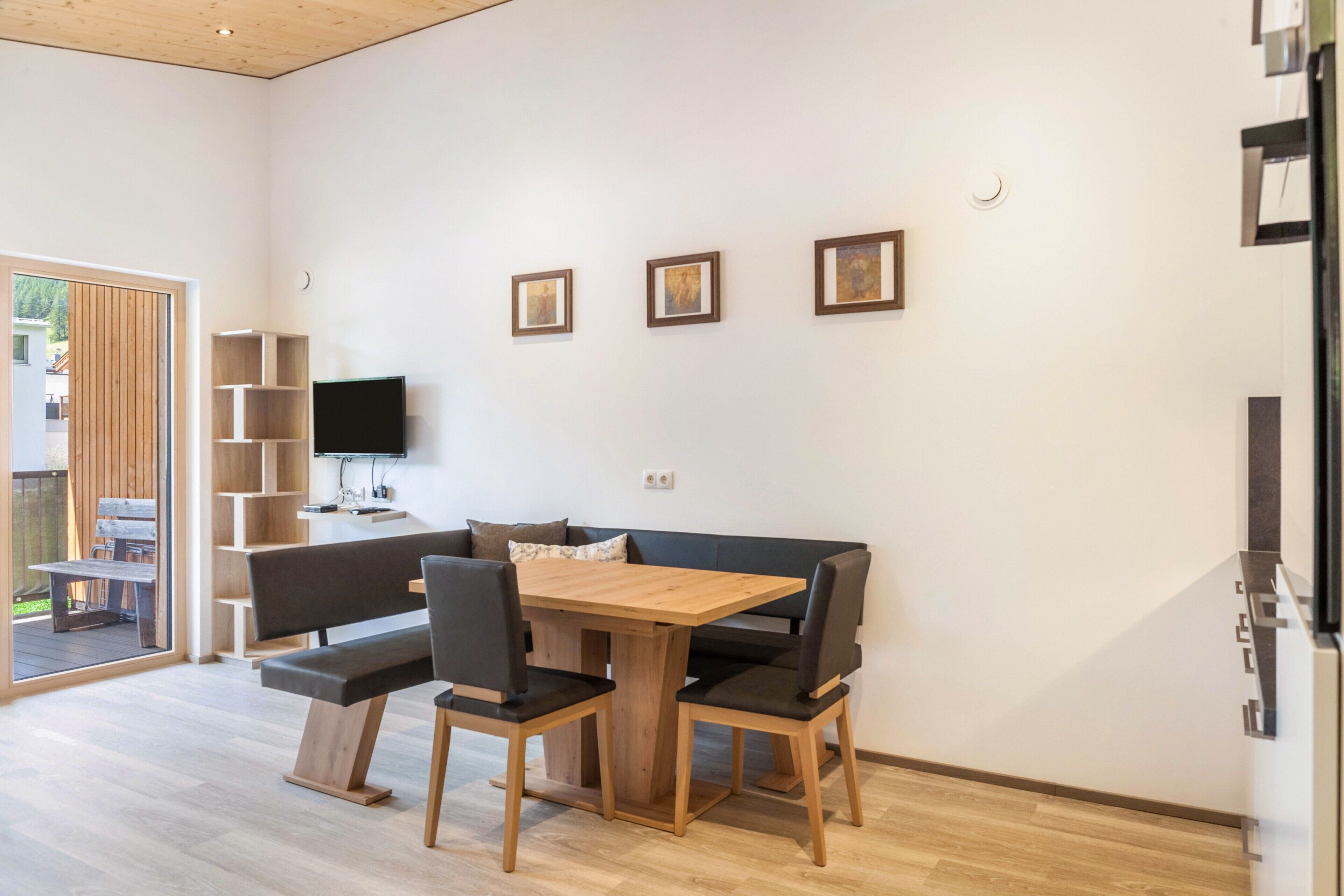 Un interior modern amb taula de dinar de fusta, seients amb coixinets negres, televisió de pantalla plana i obra d'art emmarcada a la paret.