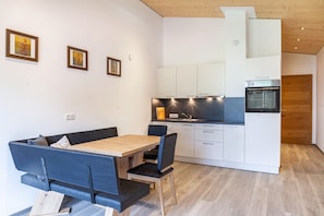 Une cuisine moderne avec des armoires blanches, un four encastré et un coin repas comprenant une table en bois et des chaises noires.