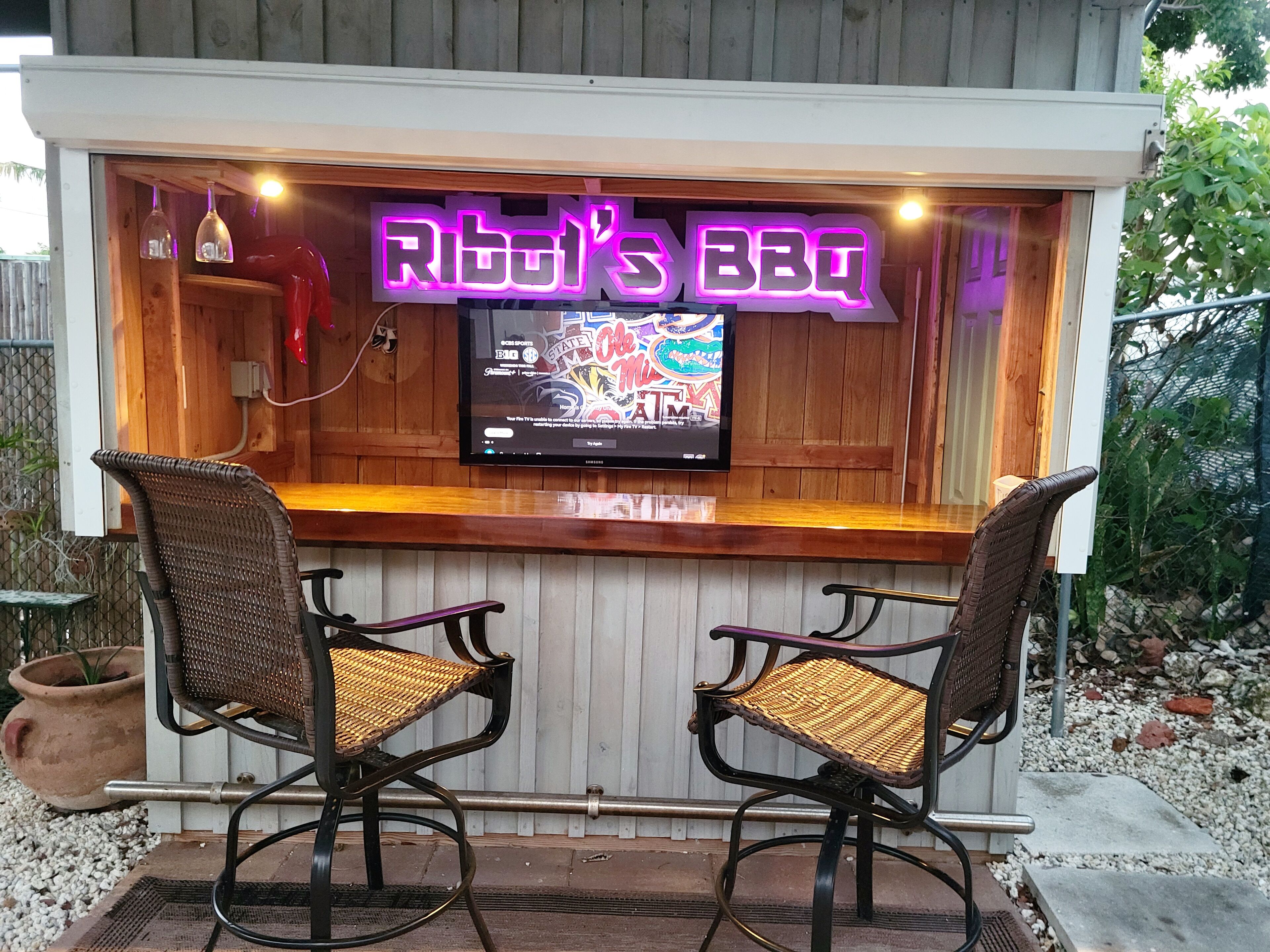 Puinen baaritiski, jossa on kaksi rottinkituolia ja neonvalomainos, jossa lukee: ”Rib’s BBQ”.