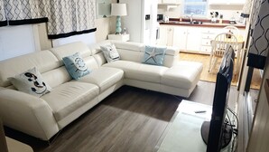 A modern living room with a beige sectional sofa, a flat-screen TV, and a kitchen area with white cabinets and a wooden countertop. - Island Paradise with private beach & private bay sunset views. (Key Largo)