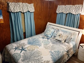 A bedroom with a bed featuring a nautical-themed bedspread, two matching curtains, and a nightstand with a lamp. - Island Paradise with private beach & private bay sunset views. (Key Largo)