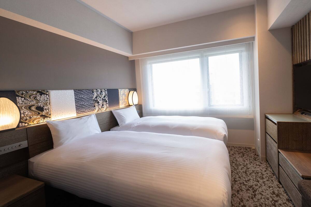 A hotel room with two beds, a large window, and a TV on a wooden cabinet.