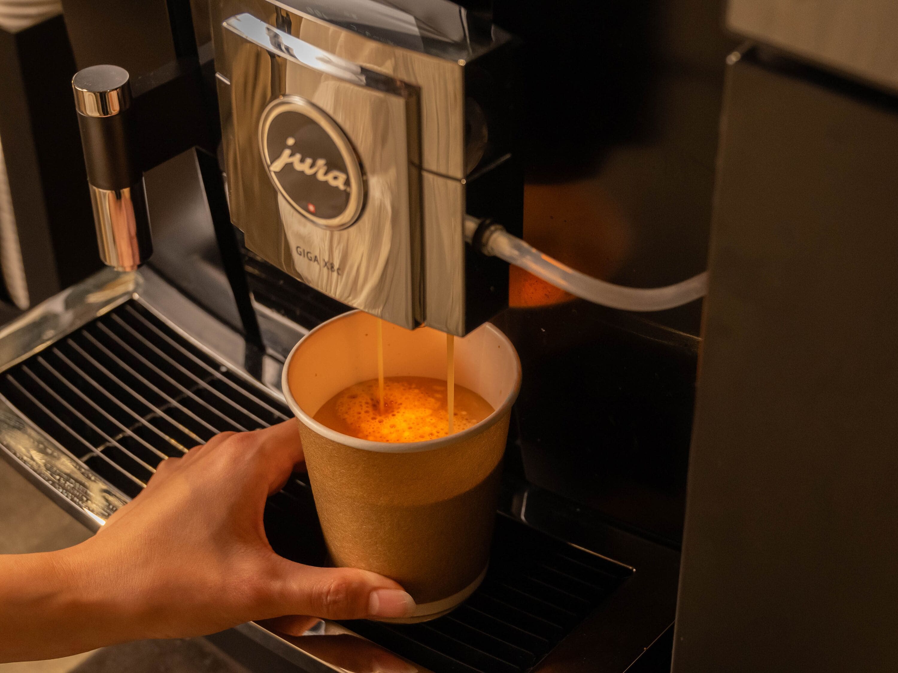 A hand holding a paper cup under a coffee machine.