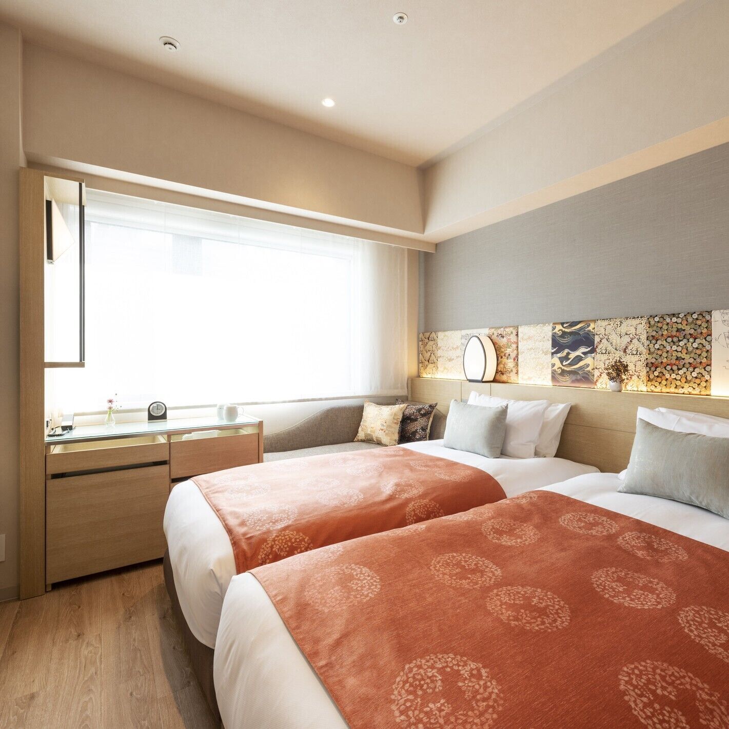Quarto de hotel com duas camas, uma escrivaninha e uma janela grande.