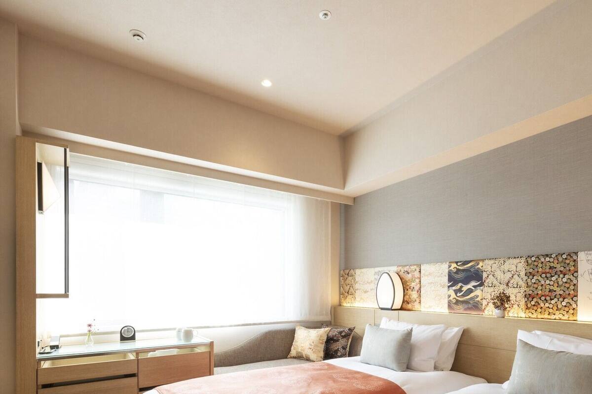 A hotel room with two beds, a desk, and a large window.