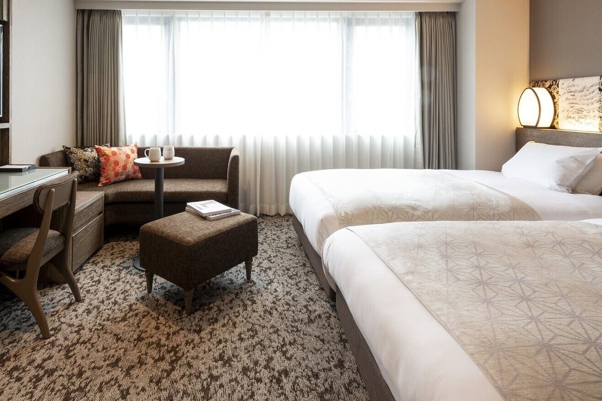 Quarto de hotel com uma cama, um sofá, uma escrivaninha e uma mesinha.