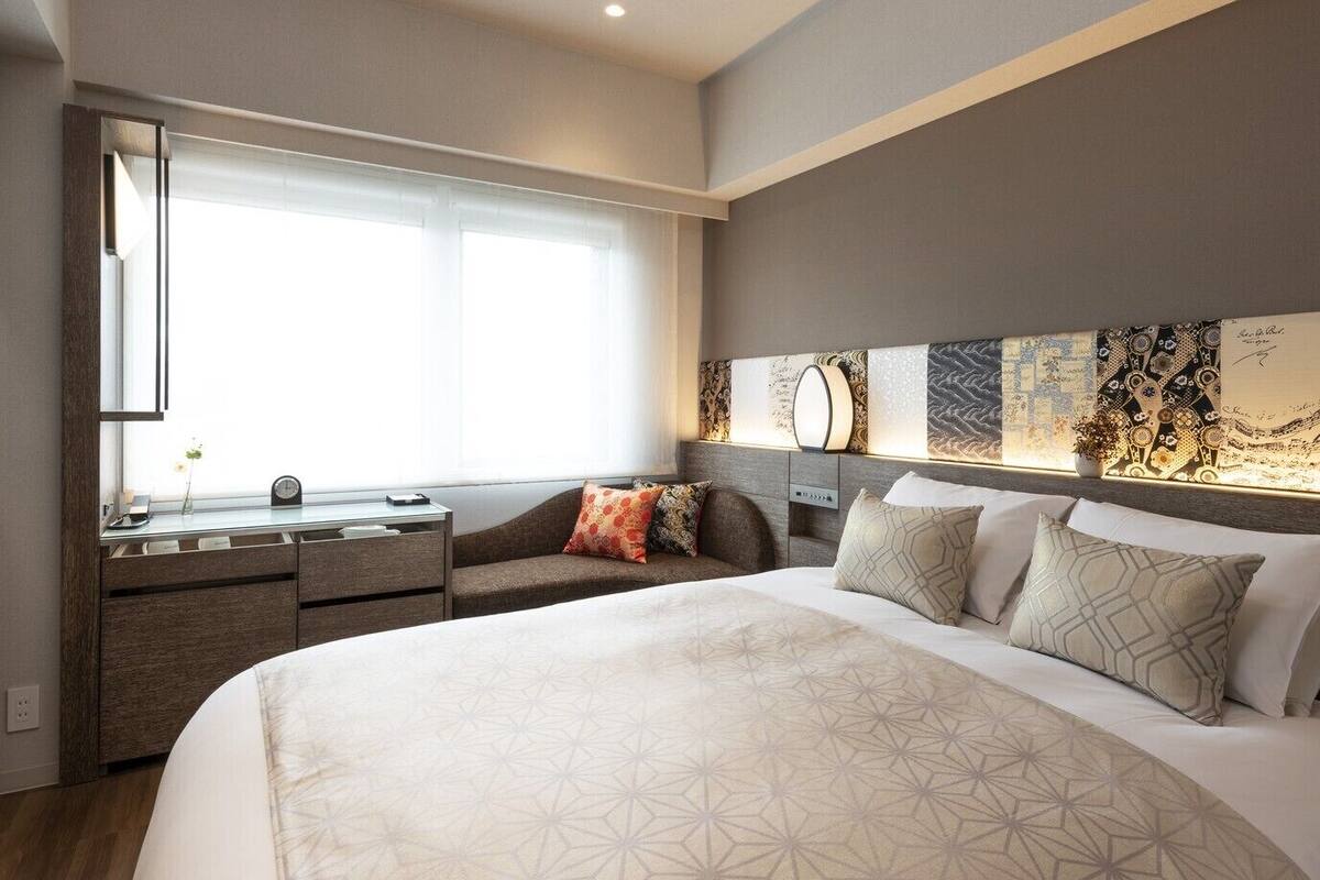 A modern hotel room with a large bed, a desk, and a window.