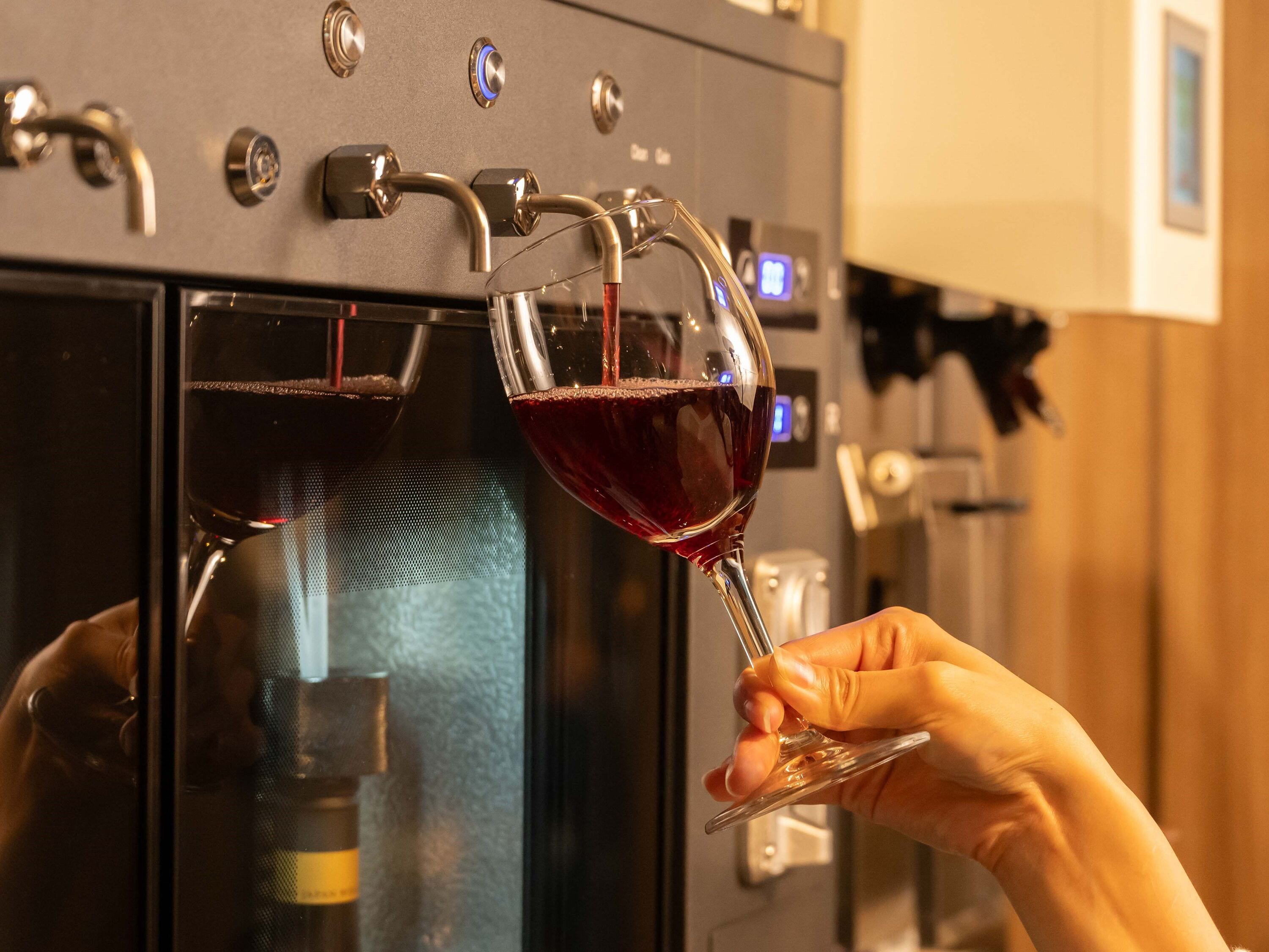 A hand holding a wine glass filled with red wine being poured from a tap.