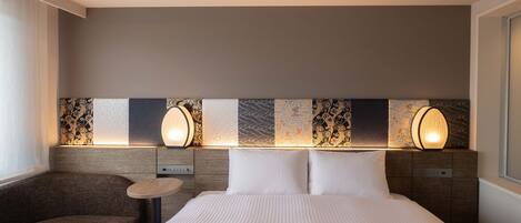 A hotel room with a large bed, two bedside lamps, a small round table, and a sofa.