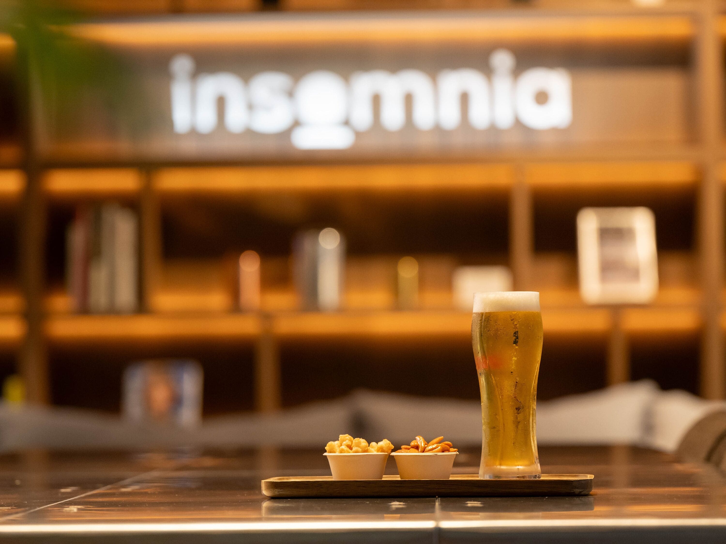 Eine Bar mit einem hohen Bierglas, zwei kleinen Schälchen Snacks und einem Holzteller.