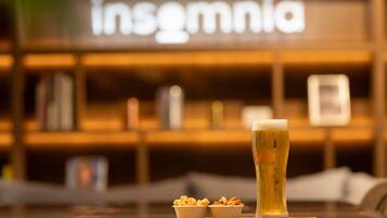 A bar setting with a tall glass of beer, two small bowls of snacks, and a wooden coaster.