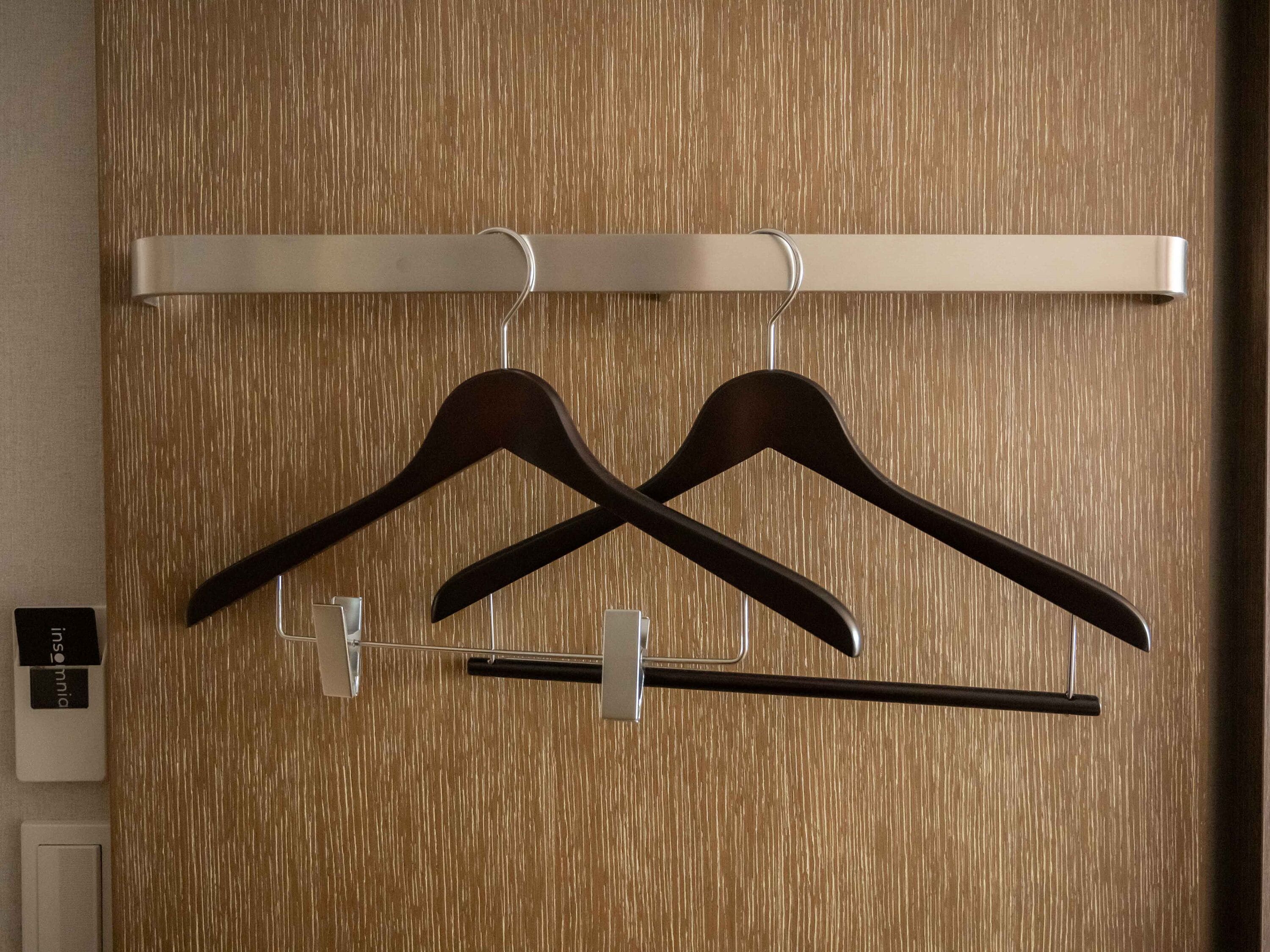 A wooden wall with a metal rack holding two dark wooden hangers.