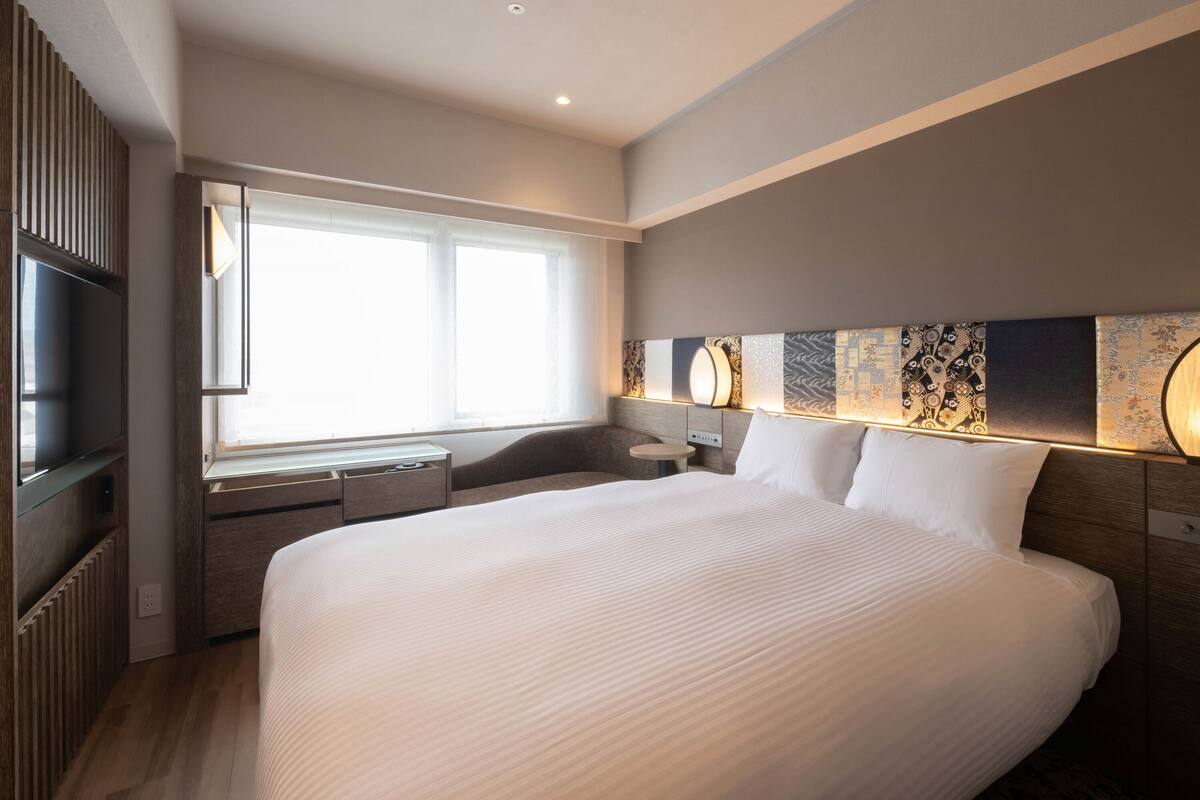 A modern hotel room with a large bed, a desk, and a TV.