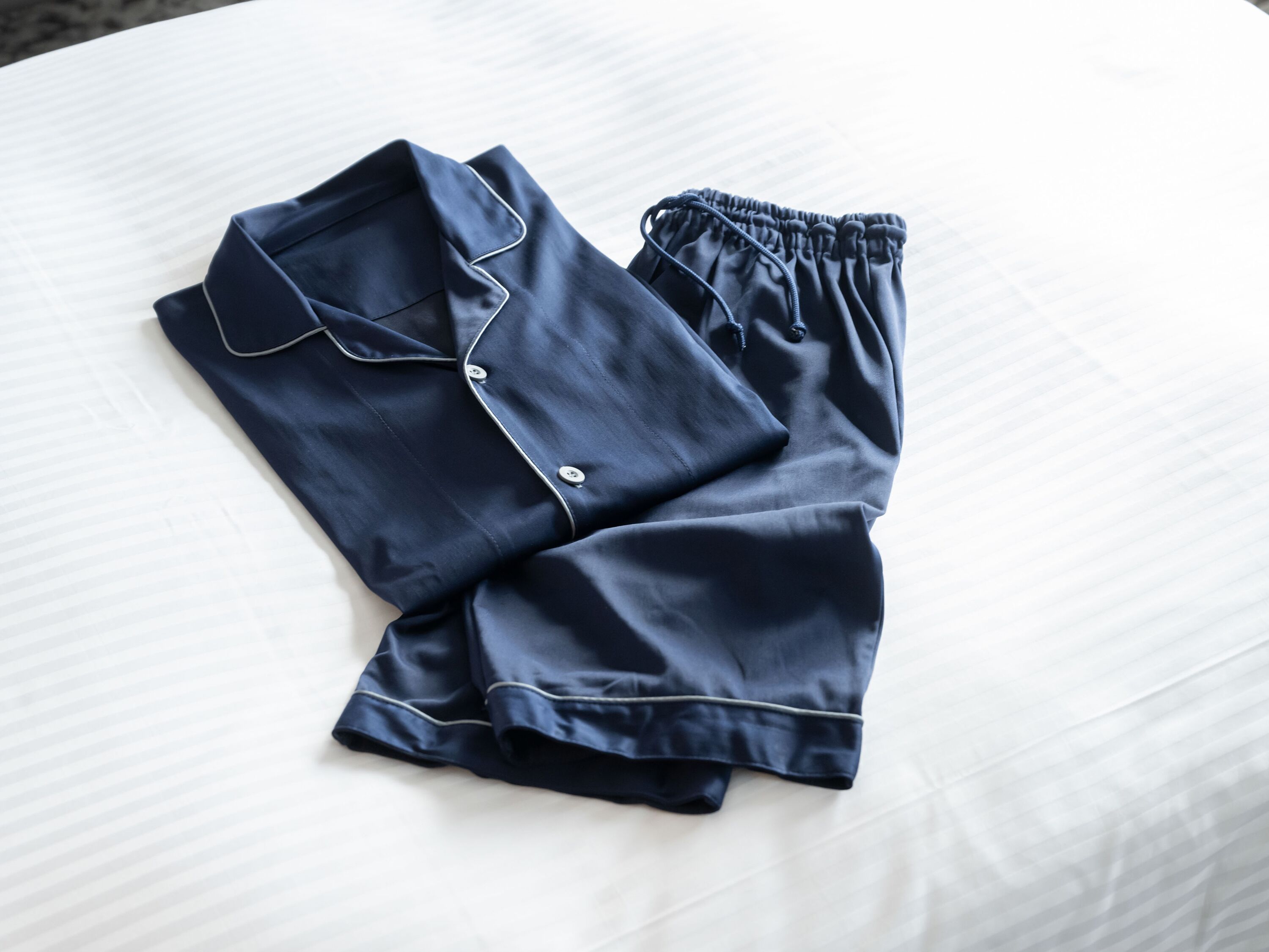 Een keurig opgevouwen marineblauwe pyjama set op een wit bed.