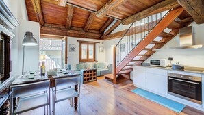 A spacious kitchen with wooden beams, a dining area with chairs, a staircase, and a view through a window.