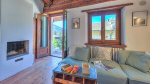 A cozy room with a wooden ceiling, a sofa with patterned cushions, a fireplace, and a view of a mountain through a window.