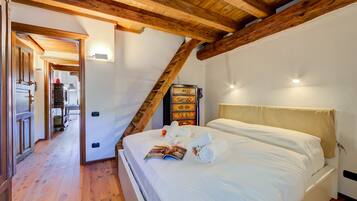 Una camera da letto con soffitto in legno, un letto con lenzuola bianche e un tavolino con una rivista.