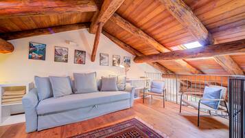 Une chambre à coucher chaleureuse, aménagée en mezzanine, avec un plafond en bois, un canapé bleu clair et un tapis à motifs.