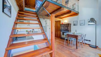 Un escalier en bois mène à une mezzanine aménagée avec une table et des chaises.