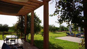 Un patio coperto con tavolo e sedie, un prato verde e poltrone relax.