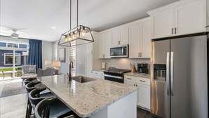 A modern kitchen with white cabinets, a stainless steel refrigerator, a microwave, and a built-in oven. - Navvy Town Neighborhood at Heritage Harbor (Ottawa)