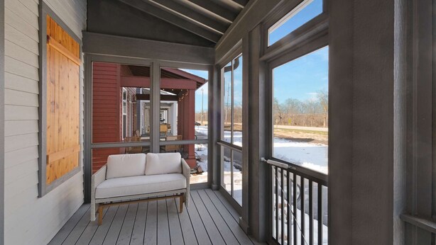 A covered porch with a white sofa, wooden deck, and large windows. - Navvy Town Neighborhood at Heritage Harbor (Ottawa)