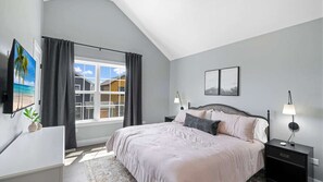 Une chambre à coucher avec un lit, des lampes de chevet, une télévision et une vue sur les maisons par la fenêtre.