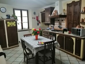 Una cocina con una mesa de comedor, sillas, un reloj, armarios, un microondas y una estufa.