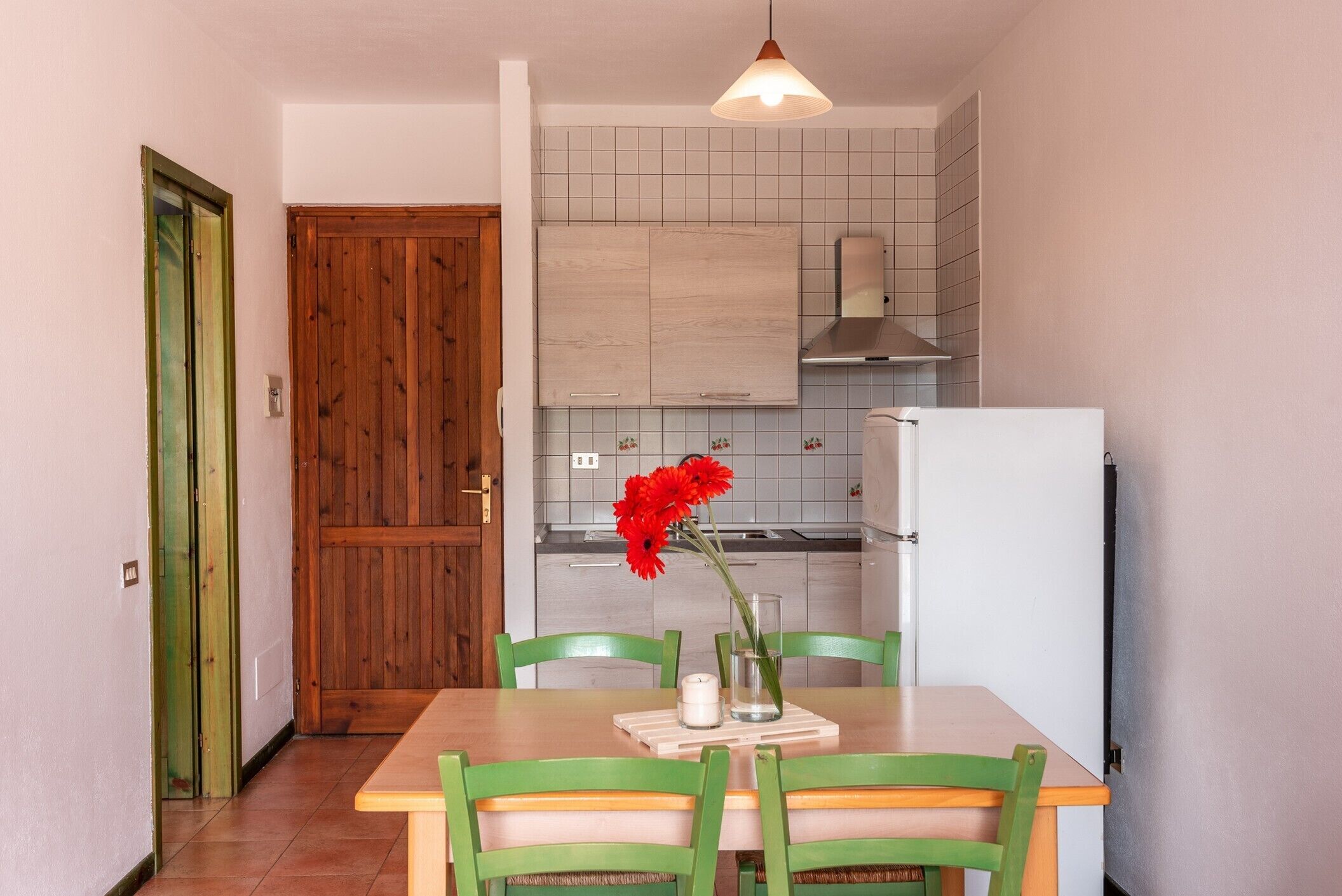 A compact kitchen with a wooden door, a dining table with chairs, and a hanging light fixture.