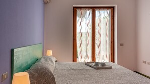 A bedroom with a bed, a nightstand, a lamp, a window with curtains, and a tray with a cup and saucer on the bed.