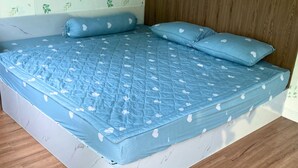 A bed with a blue quilt and matching pillows, a wooden headboard, and a wall with a leafy pattern.