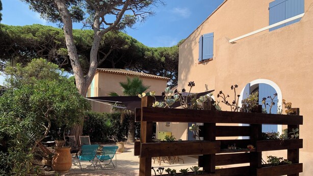 A wooden planter with various plants, a sandy ground, a blue chair, and a building with blue shutters in the background. - 10 pax, Family friendly, 2 mins walk to the beach, sea view. (Hyères)