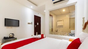 A hotel room with a large bed, a TV mounted on the wall, a window with a view of the bathroom, and a door leading to another room. - Spring Airport Hotel (Ho Chi Minh City)