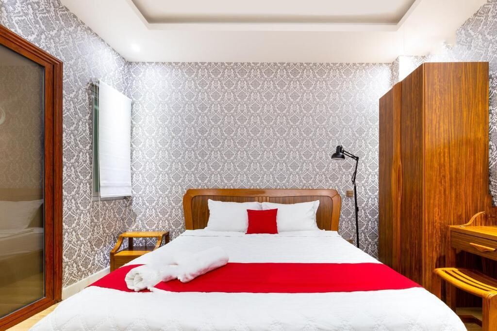 A neatly made bed with a red and white bedspread, a wooden headboard, and a white towel on the side.