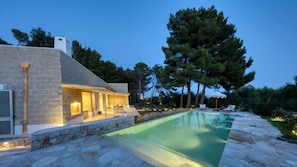 Uma casa moderna com piscina, paredes de pedra e um espaço de varanda com mobiliário de exterior.