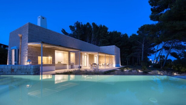 Une maison moderne dotée d’une piscine, d’une façade en pierre et d’un patio aménagé avec du mobilier d’extérieur.