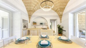Un coin repas avec une table dressée pour quatre personnes, une cuisine en arrière-plan et un plafond en pierre.