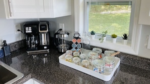 Et køkken med hvide skabe, kaffemaskine, elkedel og en bakke med krukker.