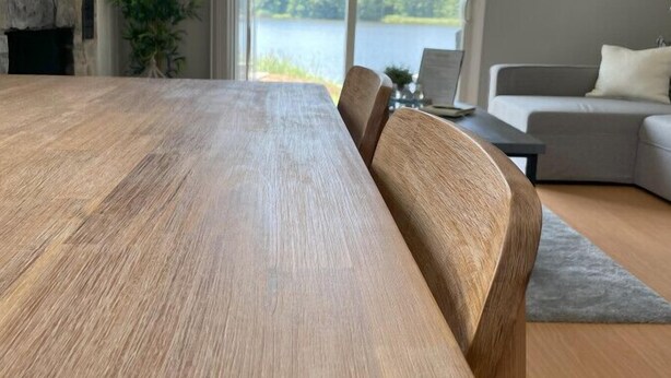 En moderne stue med et stort træspisebord, en stenkamin, en sofa og udsigt til en sø gennem store vinduer.