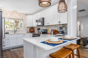 A modern kitchen with white cabinetry, a central island, and a dining area with stools.