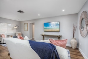 A modern living room with a white sofa, a blue throw blanket, and a painting of a beach scene.