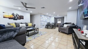 A modern living room with grey sofas, a coffee table, and a dining area with chairs and a table. - 3BR retreat w/ private fence yard • 16 min to Siesta Key (Sarasota)