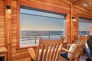 A cabin with wooden walls, large windows, and two wooden chairs with cushions.