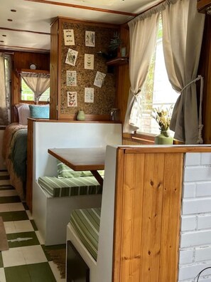 A cozy cabin interior with a wooden bench, a bulletin board with pictures, and a window with curtains.