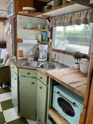 A compact kitchen with a sink, a coffee maker, and a window with a view of greenery.