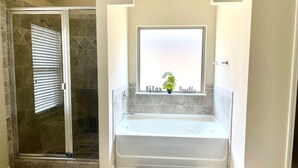 Une salle de bain avec une douche à parois de verre, une baignoire blanche et une fenêtre agrémentée d’une plante.