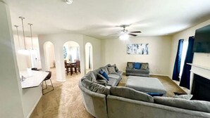 Un salon spacieux avec un grand canapé d’angle, une cheminée et un coin repas comprenant une table et des chaises.