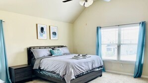 Une chambre à coucher avec un lit, des tables de chevet, un ventilateur de plafond et une fenêtre avec des rideaux.